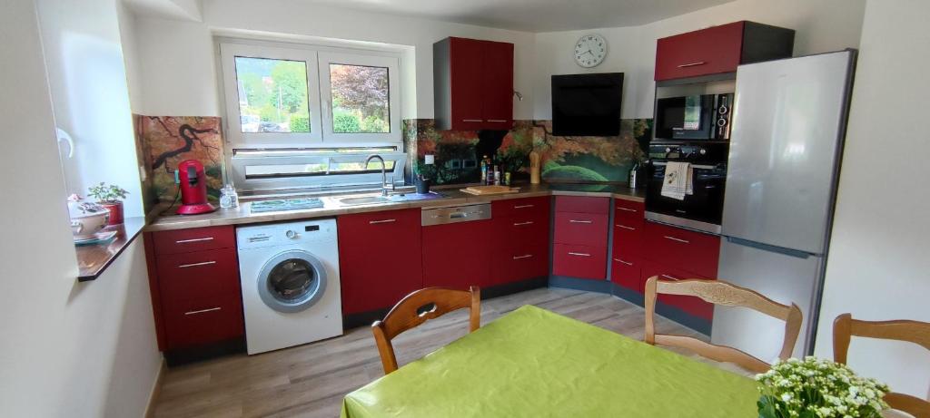 une cuisine avec des placards rouges, une table et un lave-linge dans l'établissement Le gîte de Philippe, Calme et spacieux, à Eschbach-au-Val