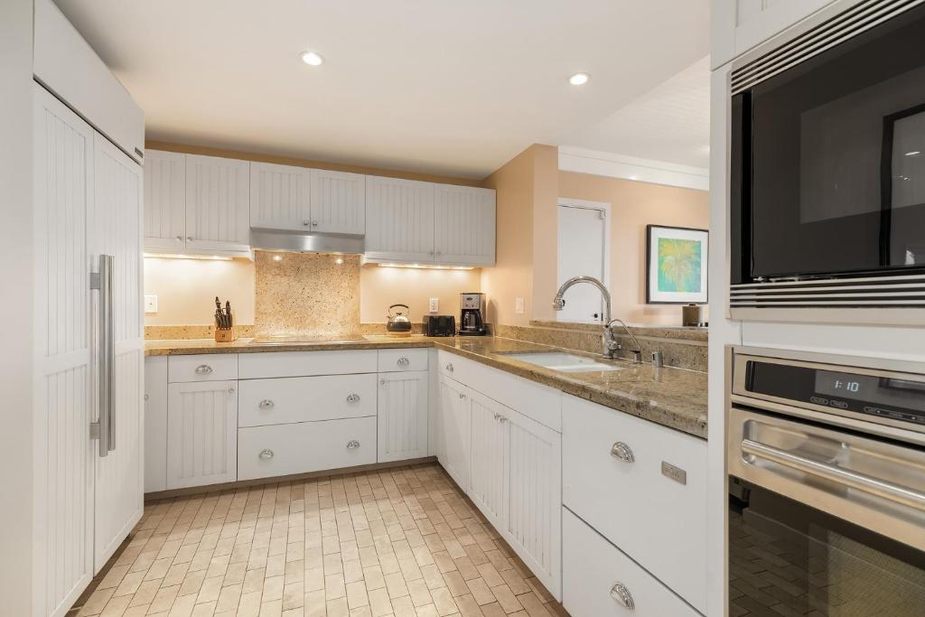 a kitchen with white cabinets and a sink and a tv at Turtle Bay Villas in Kahuku
