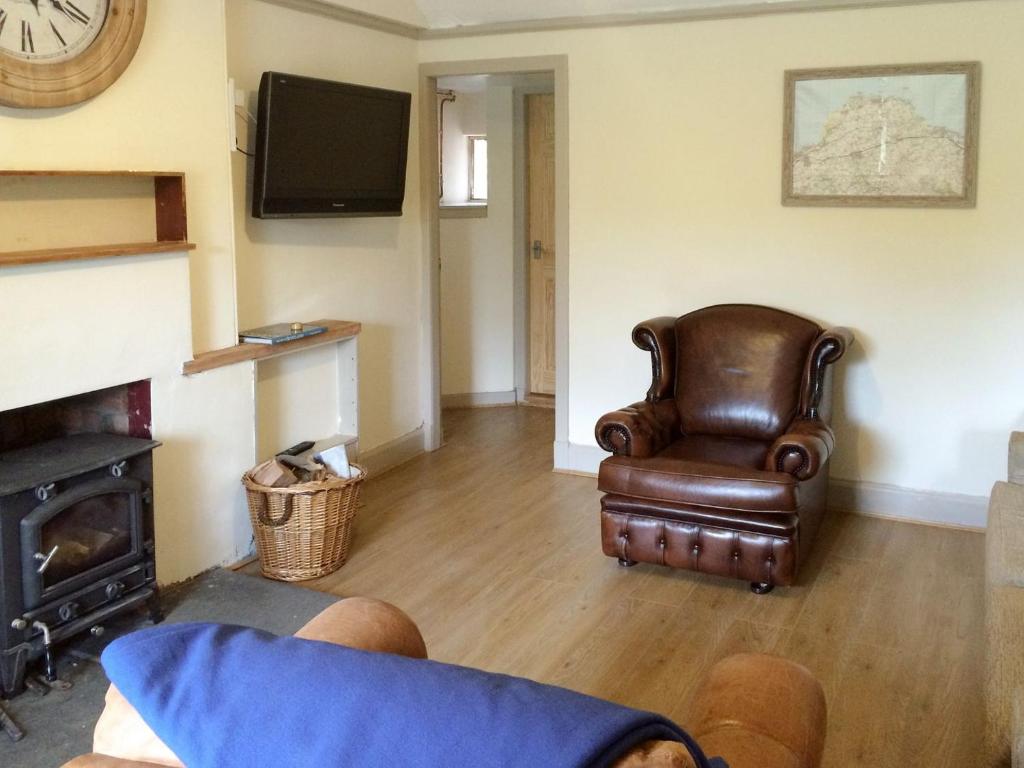 a living room with a leather chair and a fireplace at Cauldside West Cottage in Whitekirk