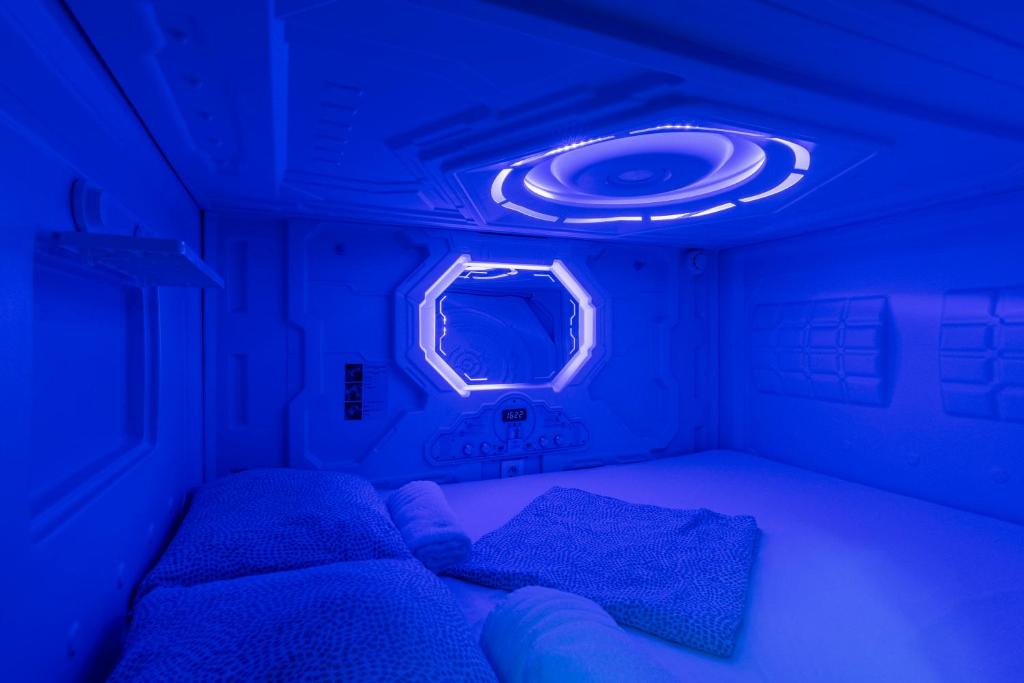 Habitación pequeña con 2 camas y luz azul en OXYGEN HOSTEL Capsula, en Madrid