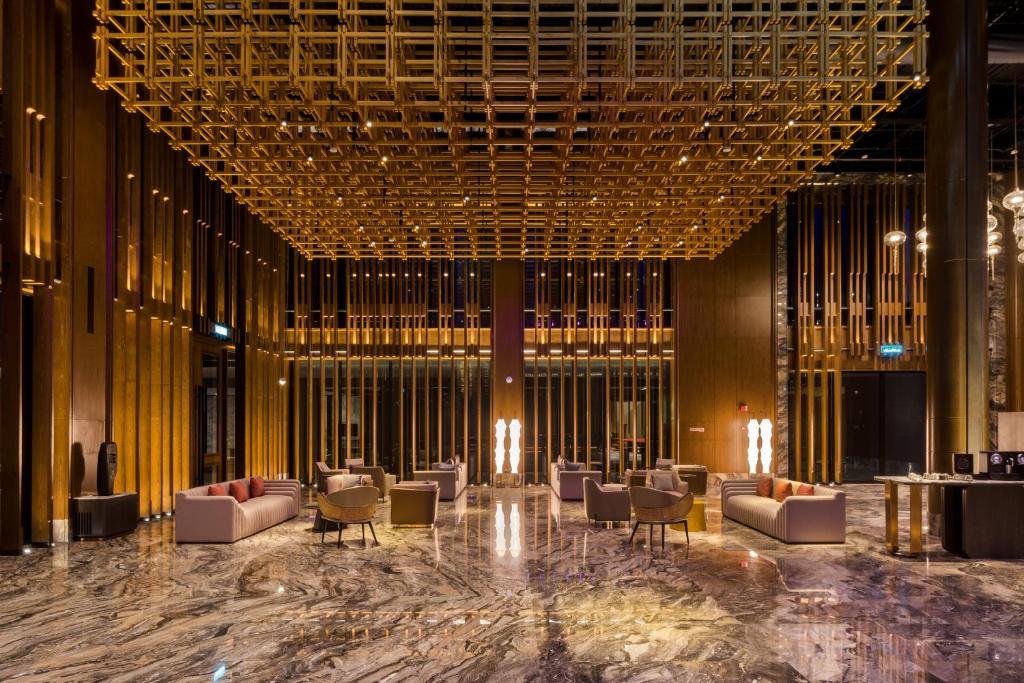 A spacious lobby lounge arranged with sofas and armchairs beneath a gold geometric ceiling.