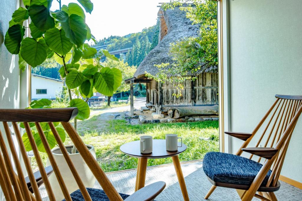 Zimmer mit 2 Stühlen, einem Tisch und einem Fenster in der Unterkunft CURIO Shirakawago in Shirakawa-gō