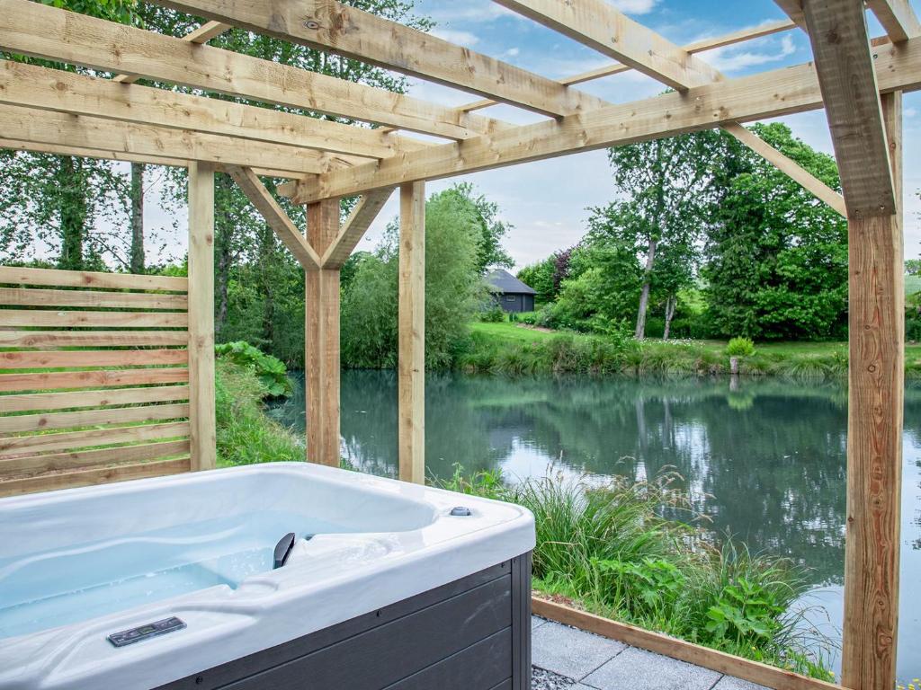 a bath tub in front of a river with a wooden pergola at Moor Hen Shepherd Hut - Uk33888 in Cullompton