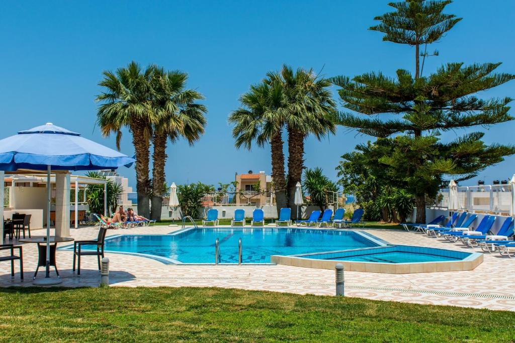 een zwembad met palmbomen en een blauwe parasol bij Manolis Apartments in Malia