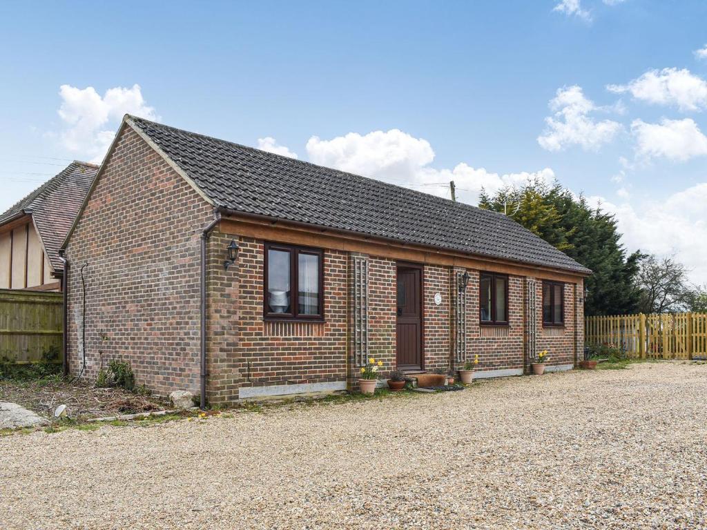 a brick house on a gravel road with a fence at Honeypot Cottage in Maresfield