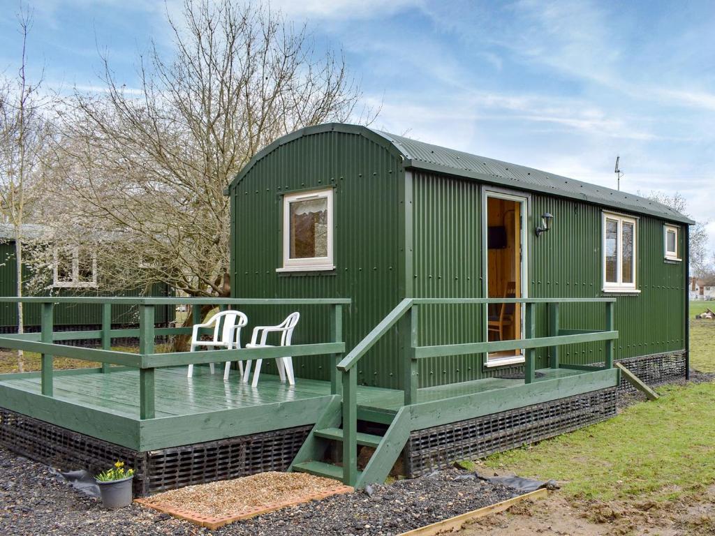 uma pequena casa verde com um alpendre e um deque em Shepherds Hut 1 At Laddingford - Uk32531 em Yalding