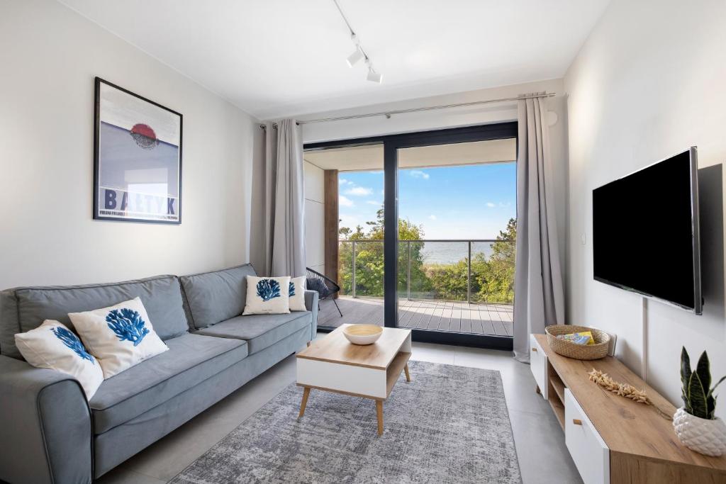 a living room with a gray couch and a large window at Apartament Natural 306 z widokiem na morze in Darłówko