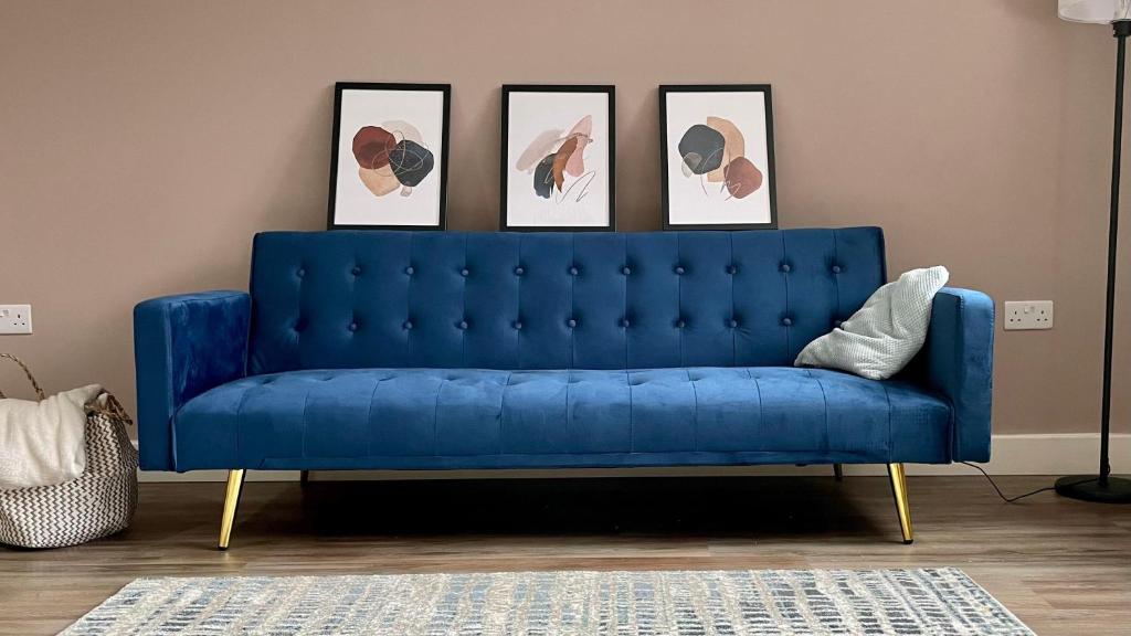 a blue couch in a living room with four pictures at Lovely 2 Bedroom Serviced Apartment with Parking in West Bromwich
