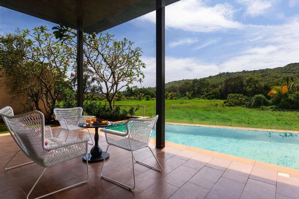 a patio with a table and chairs and a pool at StayVista at Bella Aquila with Pvt Pool & Lawn - Parra NorthGoa in Anjuna