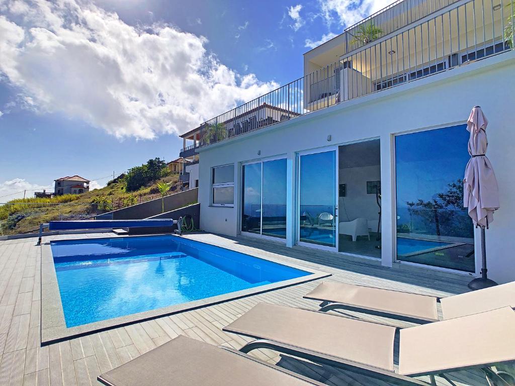 a house with a swimming pool and two chairs at Villa Piece of Heaven by LovelyStay in Estreito da Calheta