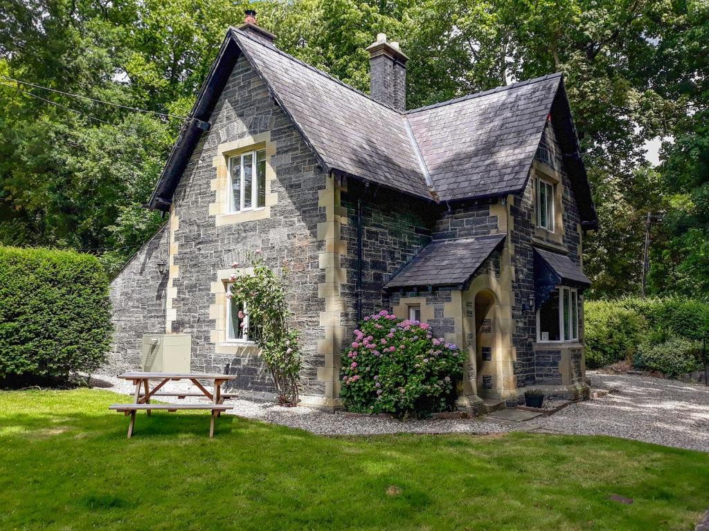 una pequeña casa de piedra con un banco en el patio en Llantysilio Lodge, en Llangollen