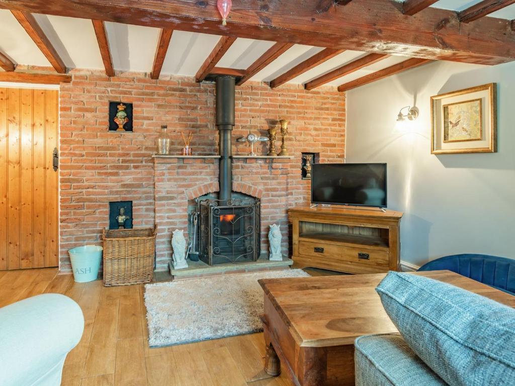 a living room with a brick fireplace and a tv at Lesta Cottage in Everingham