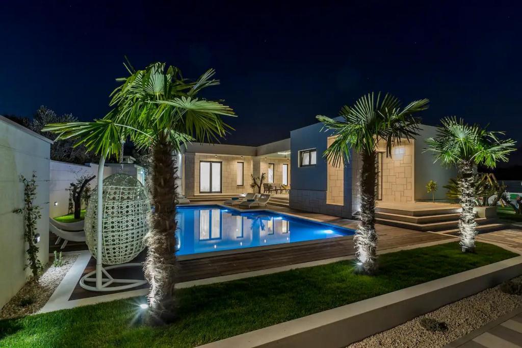 una casa con piscina por la noche con palmeras en Maglica Exclusive Residence, en Kaštela