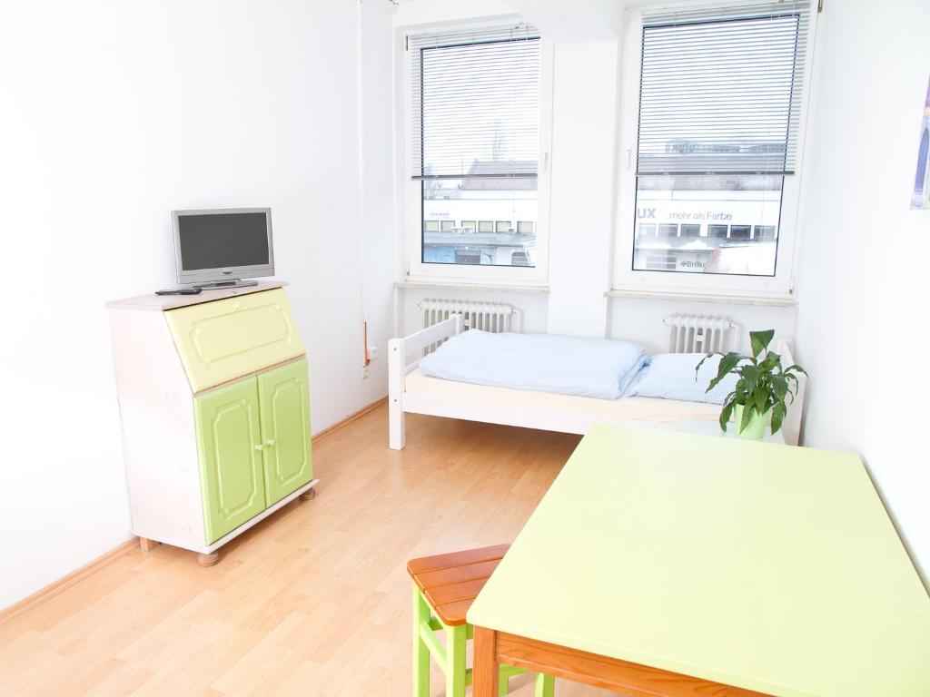 a white room with a bed and a desk with a television at PM-Rooms in Munich