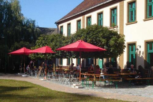 um grupo de pessoas sentadas em mesas sob guarda-chuvas vermelhos em Landgasthof Rieben em Beelitz