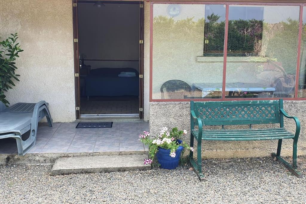 a green bench sitting in front of a door with a pot of flowers at CAMAT T1 de plain pied à la campagne in Cazaubon