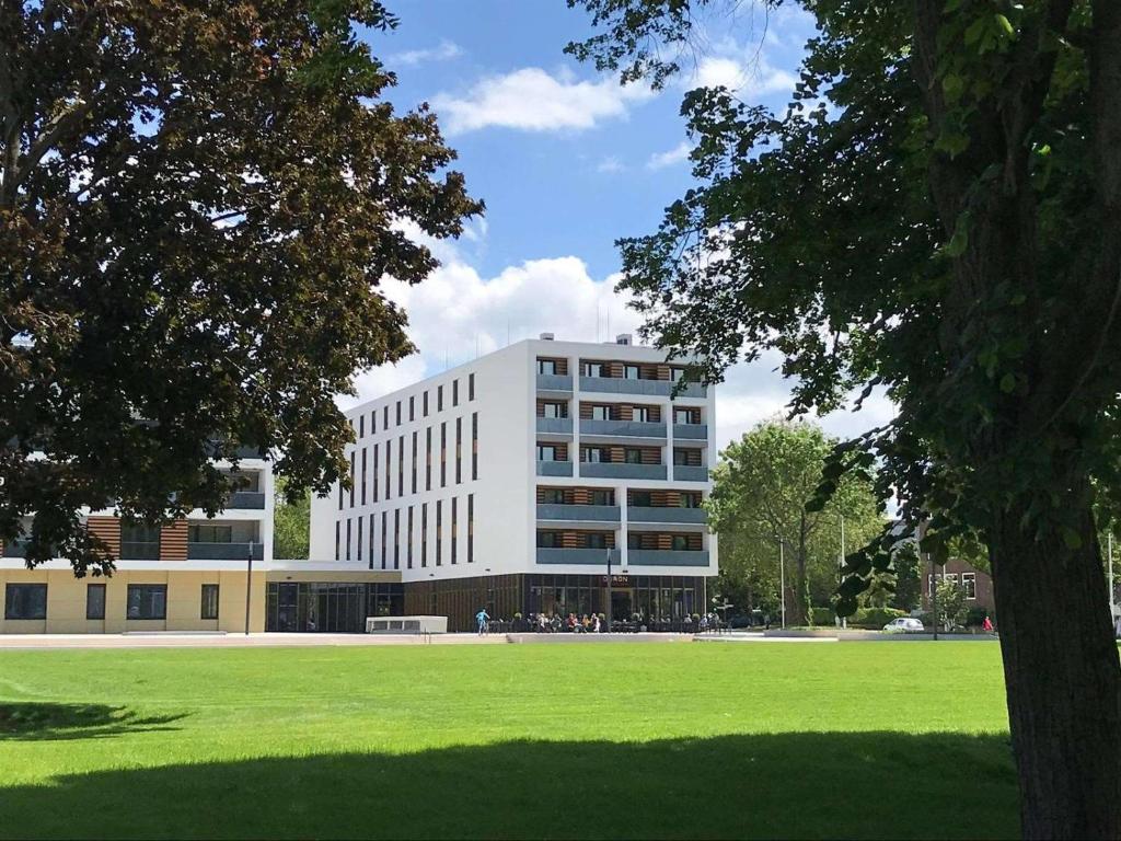 un grand bâtiment blanc avec un champ vert en face dans l'établissement Dorint Hotel Düren, à Düren