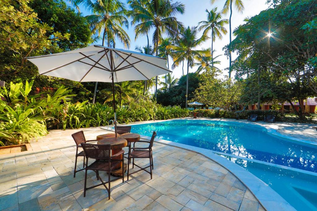 a table and chairs with an umbrella next to a swimming pool at Pousada Sitio da Prainha in Praia dos Carneiros