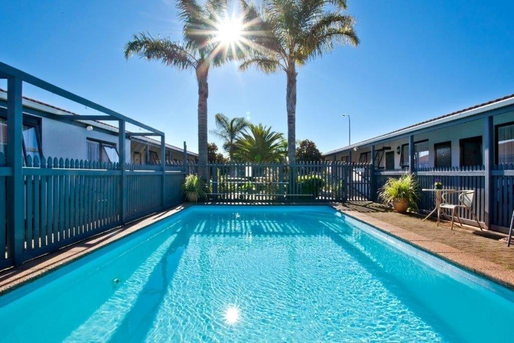 a swimming pool with palm trees and a fence at Cortez Motel in Whakatane