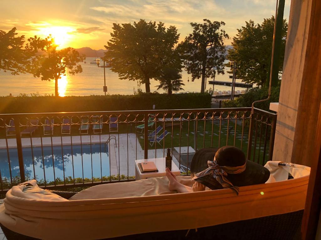 a woman sitting in a tub on a balcony with the sunset at Front Lake Apartment Rainer in Bardolino