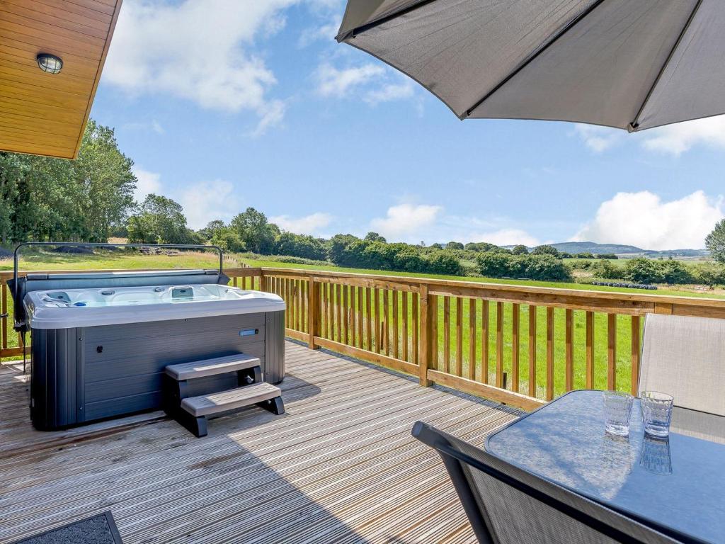 a hot tub on a deck with a table and an umbrella at Nanny Goat Lodge in Crossway Green