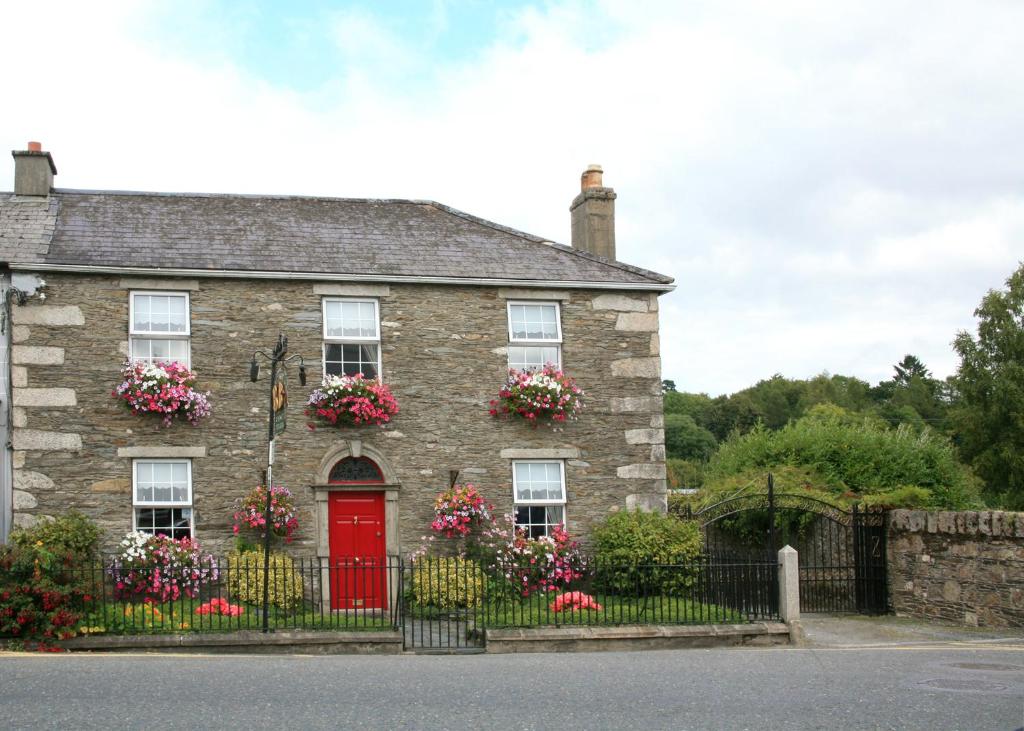 una vecchia casa in pietra con una porta rossa e fiori di Meadowside B&B a Bunclody