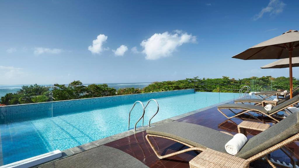 einen Pool mit Stühlen und einem Sonnenschirm in der Unterkunft Holiday Inn Bali Sanur, an IHG Hotel in Sanur