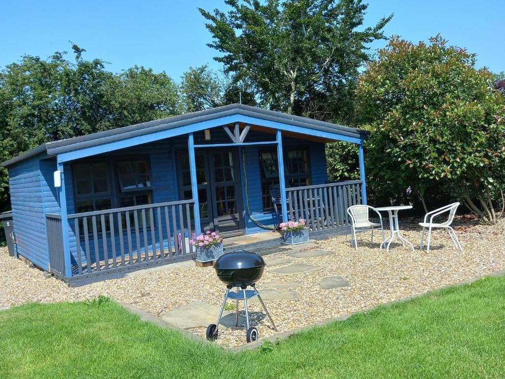a blue shed with a grill and chairs and a table at The Cabin in Elmstone