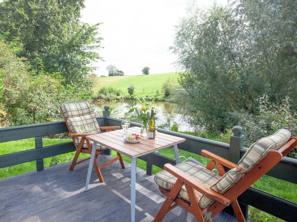 a table and chairs on a deck with a view of a river at Coot Roundhouse - Uk33890 in Cullompton