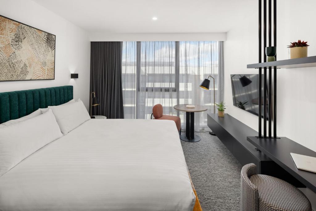 a hotel room with a white bed and a desk at The Sebel Canberra Campbell in Canberra