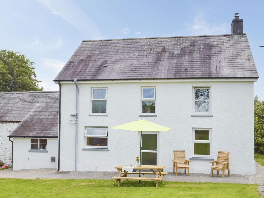 a white house with a picnic table and an umbrella at Typicca Farmhouse in Brechfa