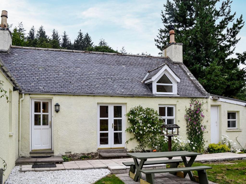 una casa de campo blanca con una mesa de picnic frente a ella en Corrennie School Cottage, en Whitehouse