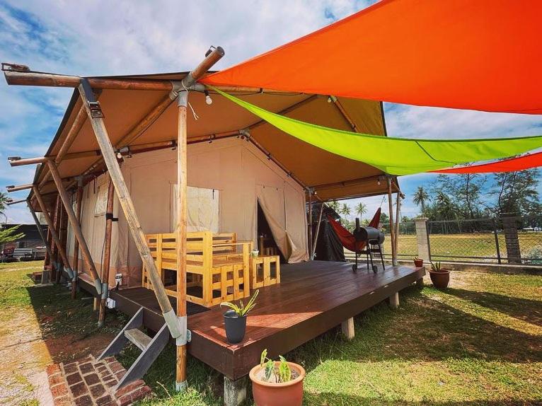 a tent with chairs and a table in a field at Rembulan Escape - Beachfront safari tent in Kampung Penarik