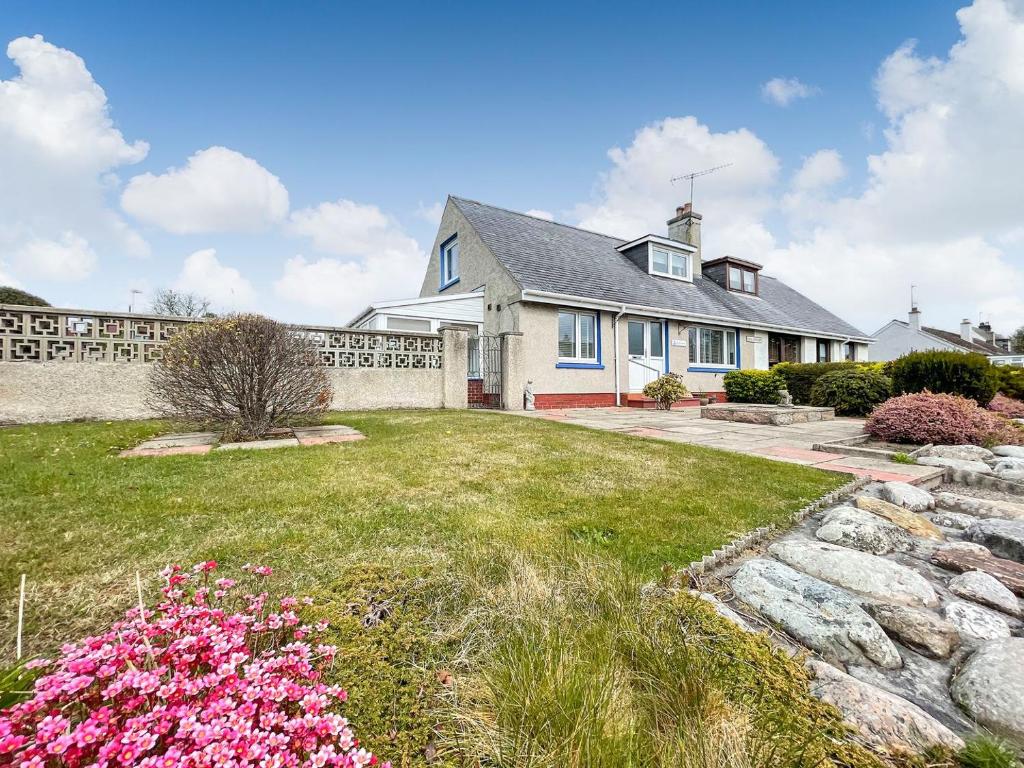 a white house with a yard with pink flowers at Iseabails House in Balintore