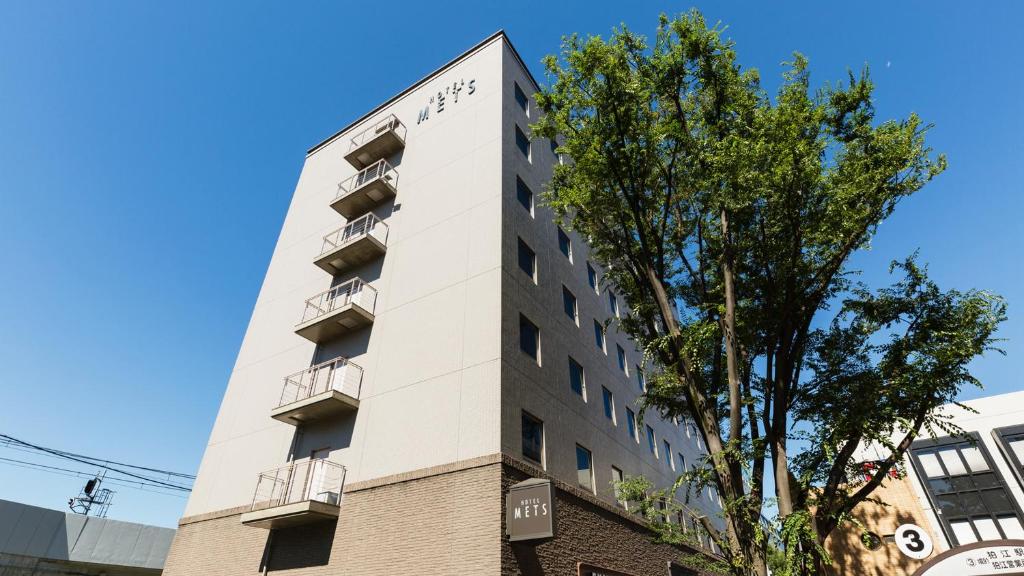 a tall white building with balconies and a tree at JR-East Hotel Mets Musashisakaii in Musashino