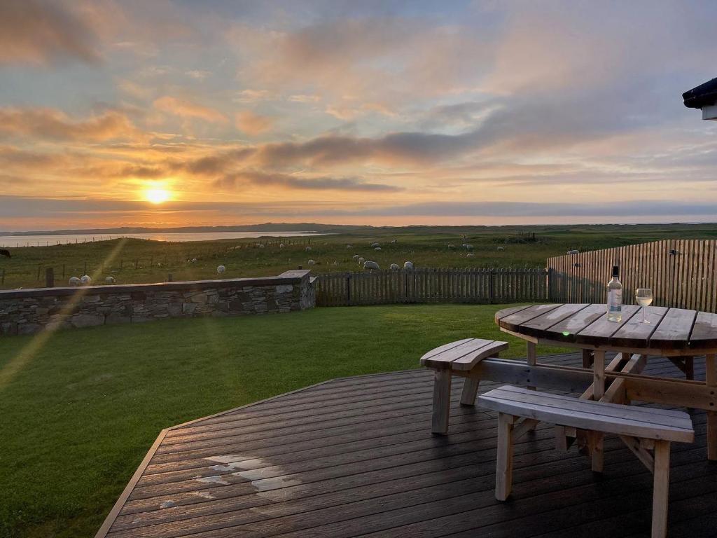 a wooden deck with a picnic table and a sunset at Clover Cottage in Sollas