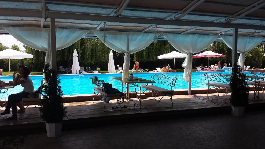 a woman sitting at a table next to a swimming pool at Hotel Racic Self-Check In in Voyvodinovo