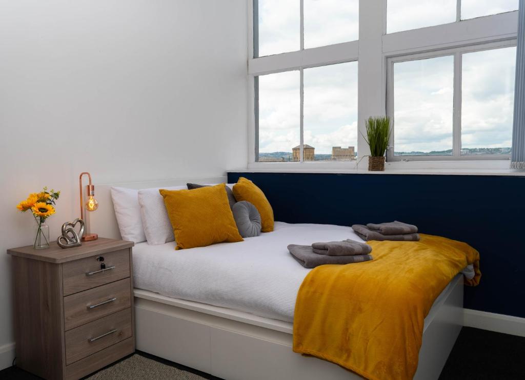 a bedroom with a bed with a yellow blanket and windows at Sky Apartments in Bradford