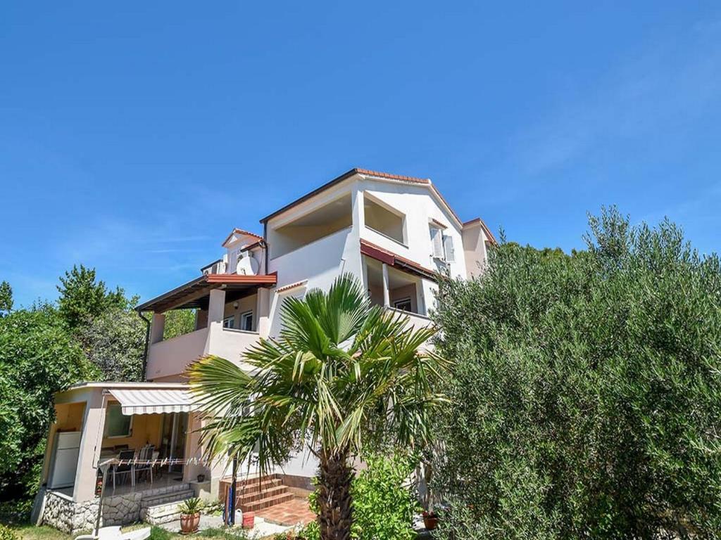 a white building with a palm tree in front of it at Apartments Jaklin in Rab