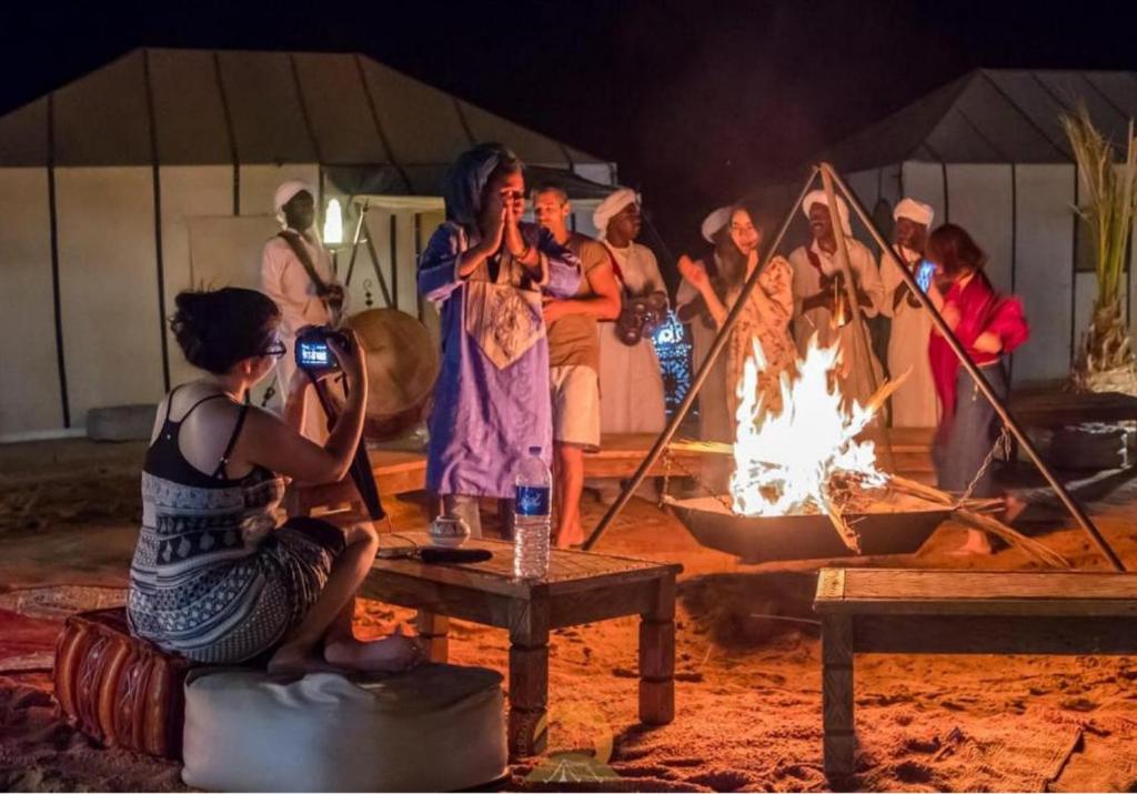 a group of people standing around a fire at Candy Camp in Merzouga