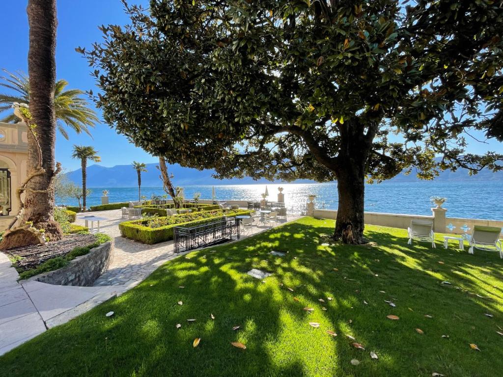 ein Park mit einem Baum und Bänken und dem Meer in der Unterkunft Hotel Villa Giulia in Gargnano