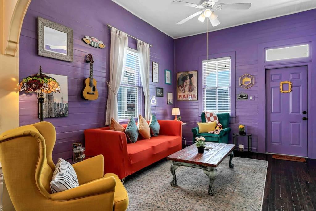 FRIENDS AIRBNB Themed 2bed 2bath walkable to all of Ybor في تامبا: غرفة معيشة مع جدران أرجوانية وأريكة حمراء وكراسي