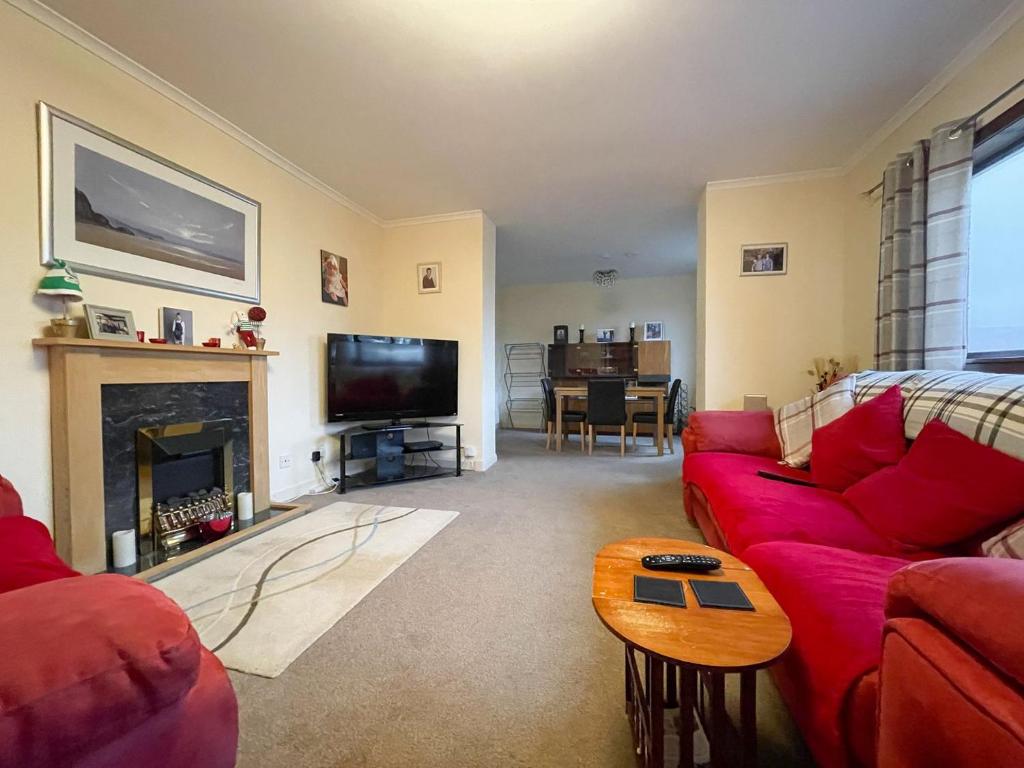 a living room with a red couch and a fireplace at Bervie Road Cottage in Kinlochbervie