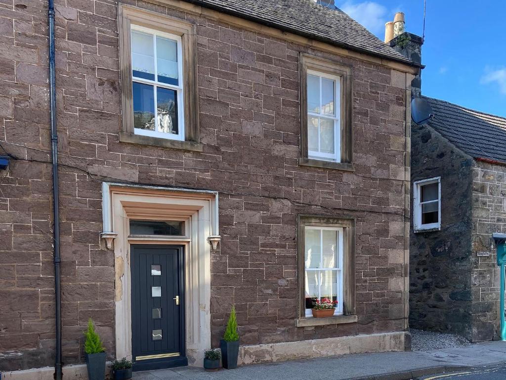 a brick house with a black door and windows at Arden House in Comrie