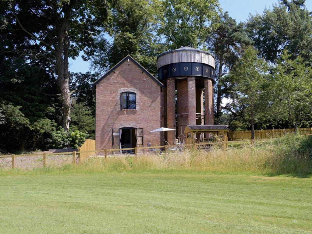 uma casa velha com uma torre de água num campo em The Pump House em Kiddemore Green