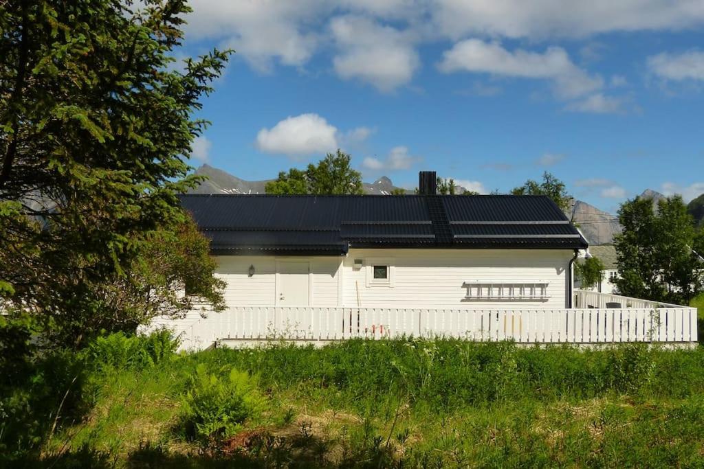 a white house with a black roof and a fence at Cozy Apartment between sea and mountains in Mefjordvær