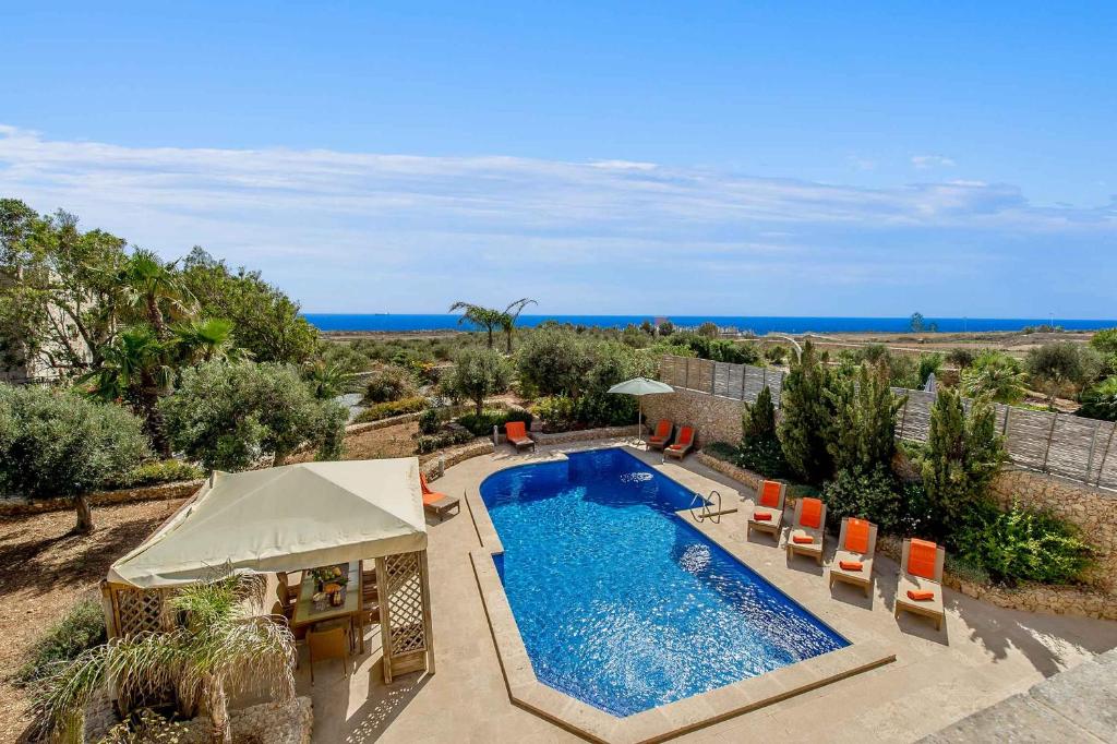 una piscina con sillas, una sombrilla y el océano en The Almonds Luxury Villa, en San Lawrenz