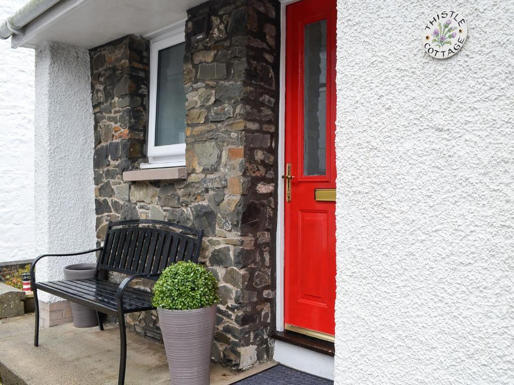 a bench sitting outside of a house with a red door at Thistle Cottage in Portpatrick