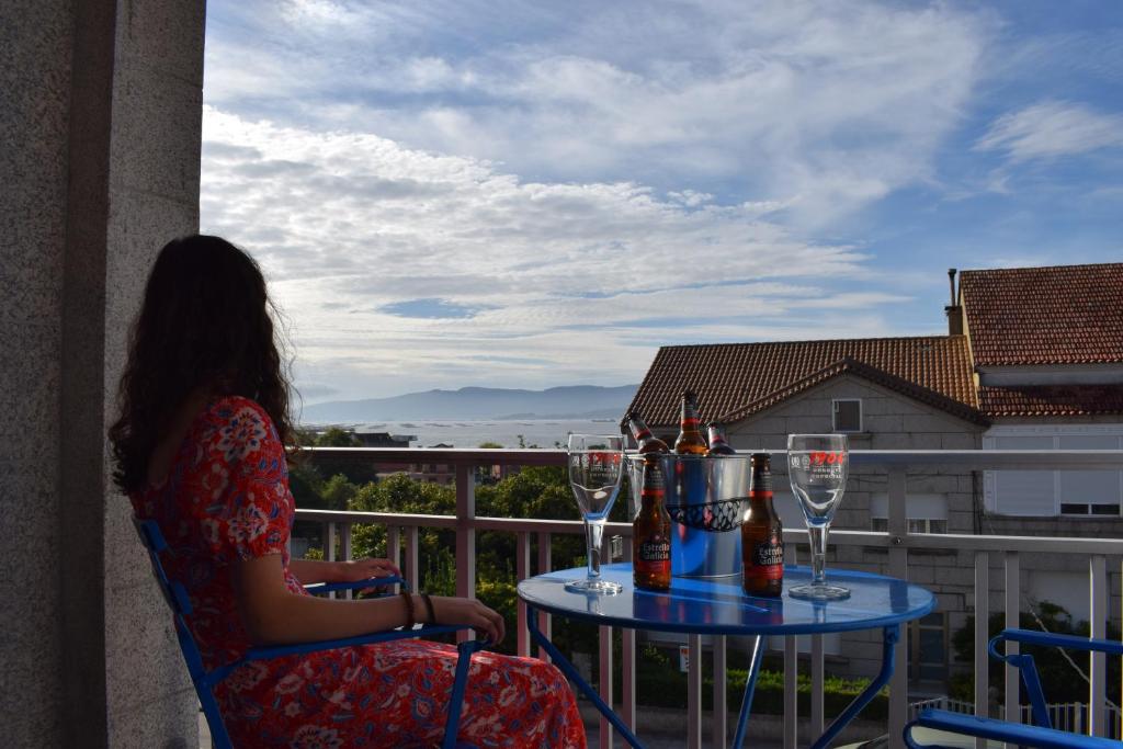 une femme assise sur une chaise sur un balcon avec des verres à vin dans l'établissement Apartamento Corcubica mirando al mar, à Vilagarcía de Arousa