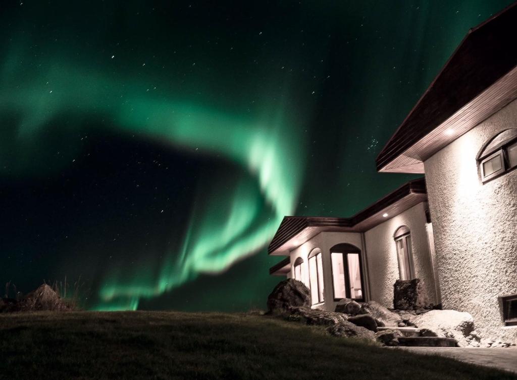 a house with the aurora in the sky next to a building at ÁLka - Cozy Room by the Sea With Private Hot Tub in Njarðvík